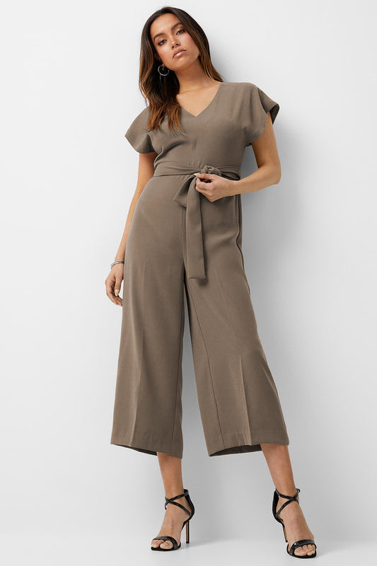 Fashion-forward woman showcasing a taupe jumpsuit with a flattering V-neckline and short sleeves. The outfit is cinched at the waist with a tie belt, leading into wide-legged cropped pants, creating a sleek silhouette