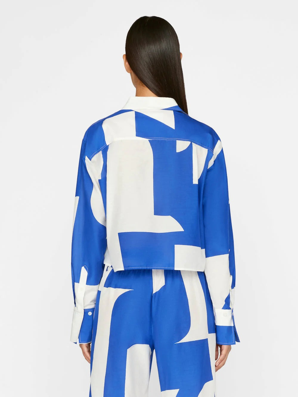 A model wears a co-ord set with a dynamic blue and white abstract wave pattern, comprising a buttoned shirt and wide-leg trousers