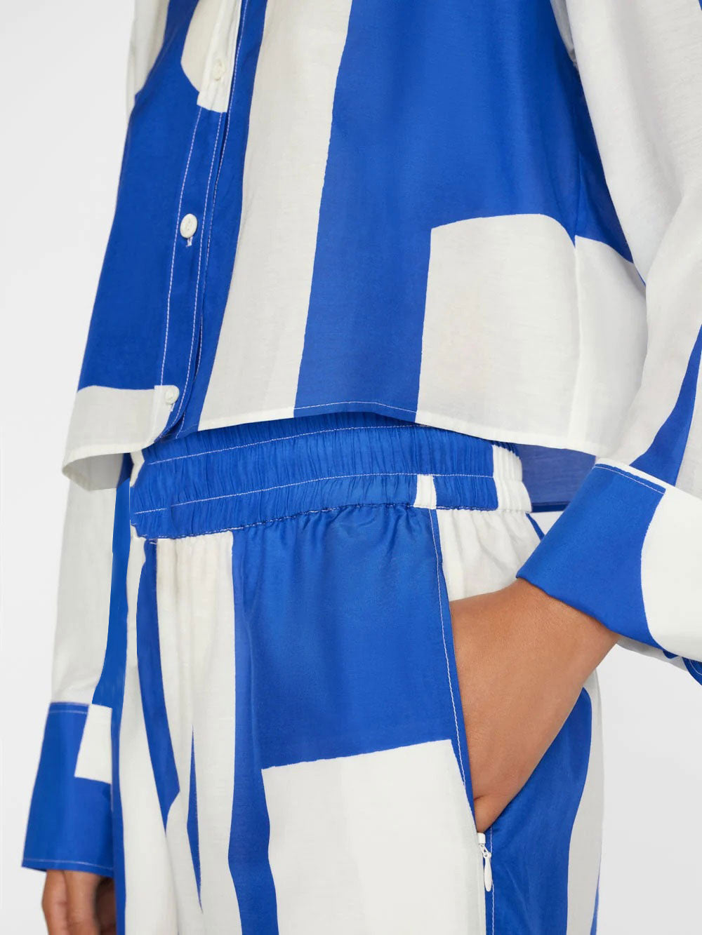 A model wears a co-ord set with a dynamic blue and white abstract wave pattern, comprising a buttoned shirt and wide-leg trousers